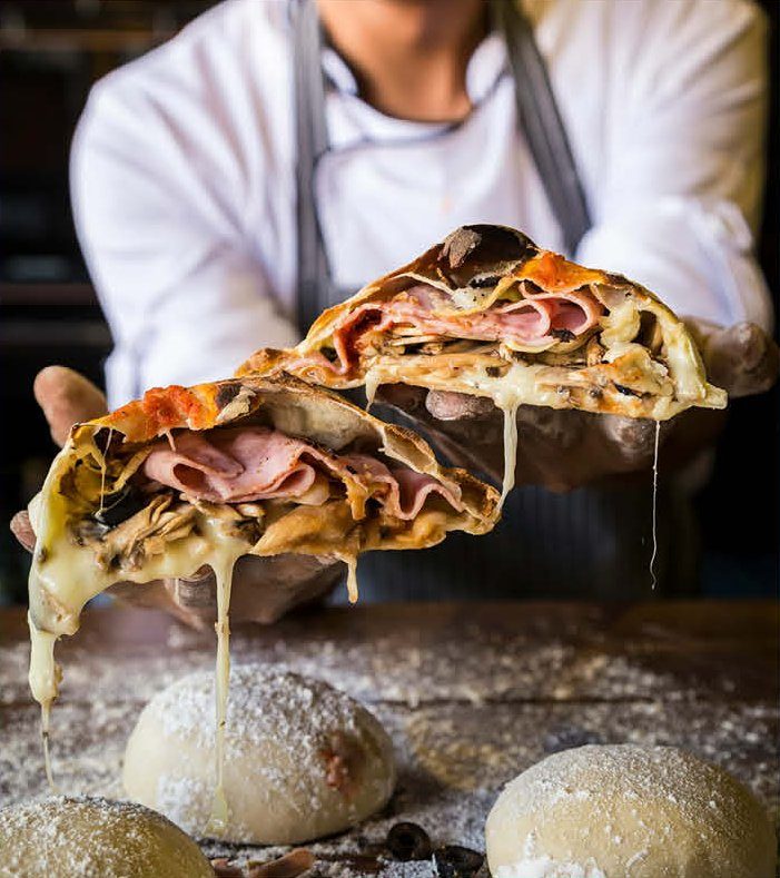 Pizzaiolo présentant une part de pizza garnie au-dessus des pâtons — la soirée pizza à partager de Toscanacci a casa